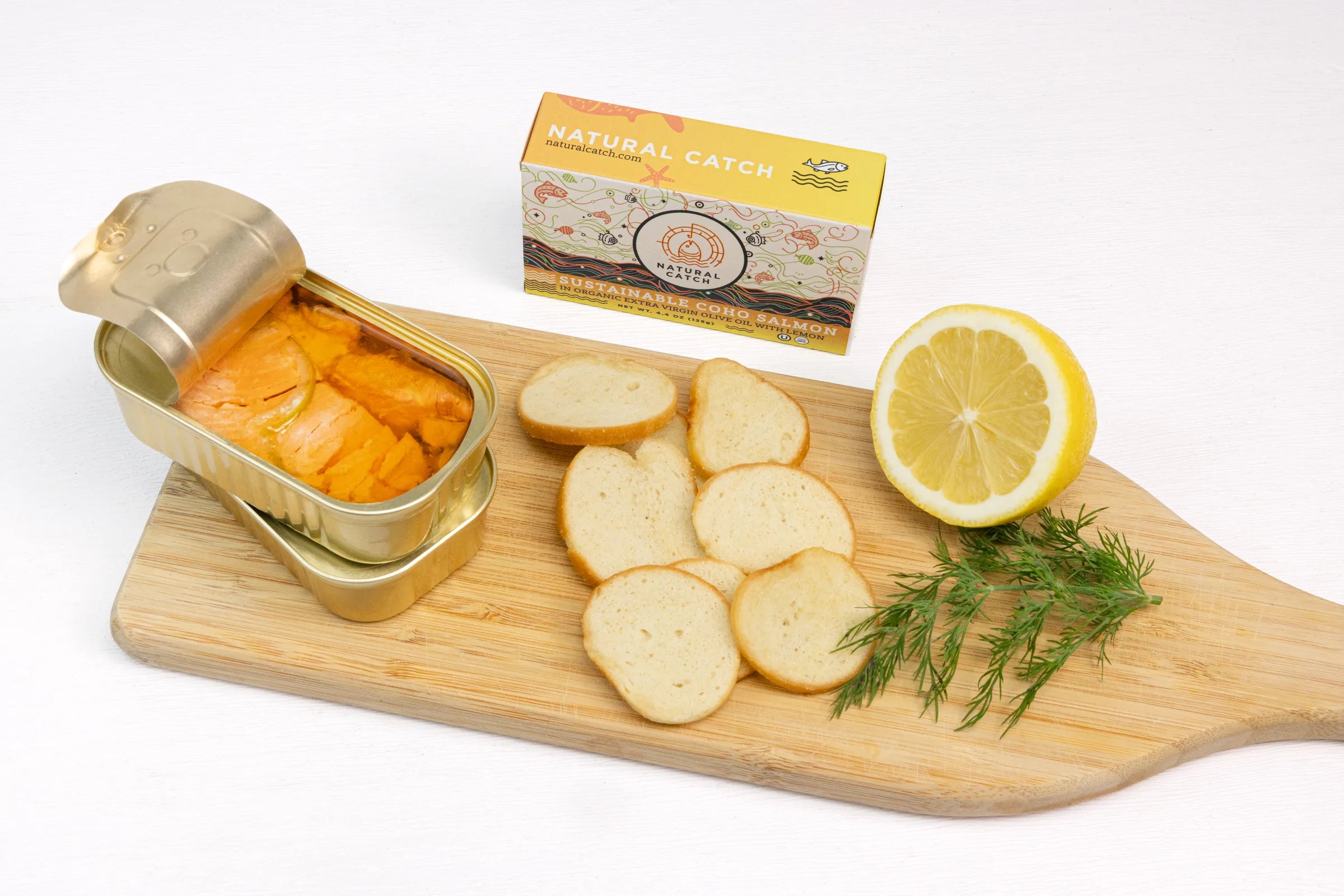 Canned Coho salmon on wooden board with crackers, lemon, dill, and product