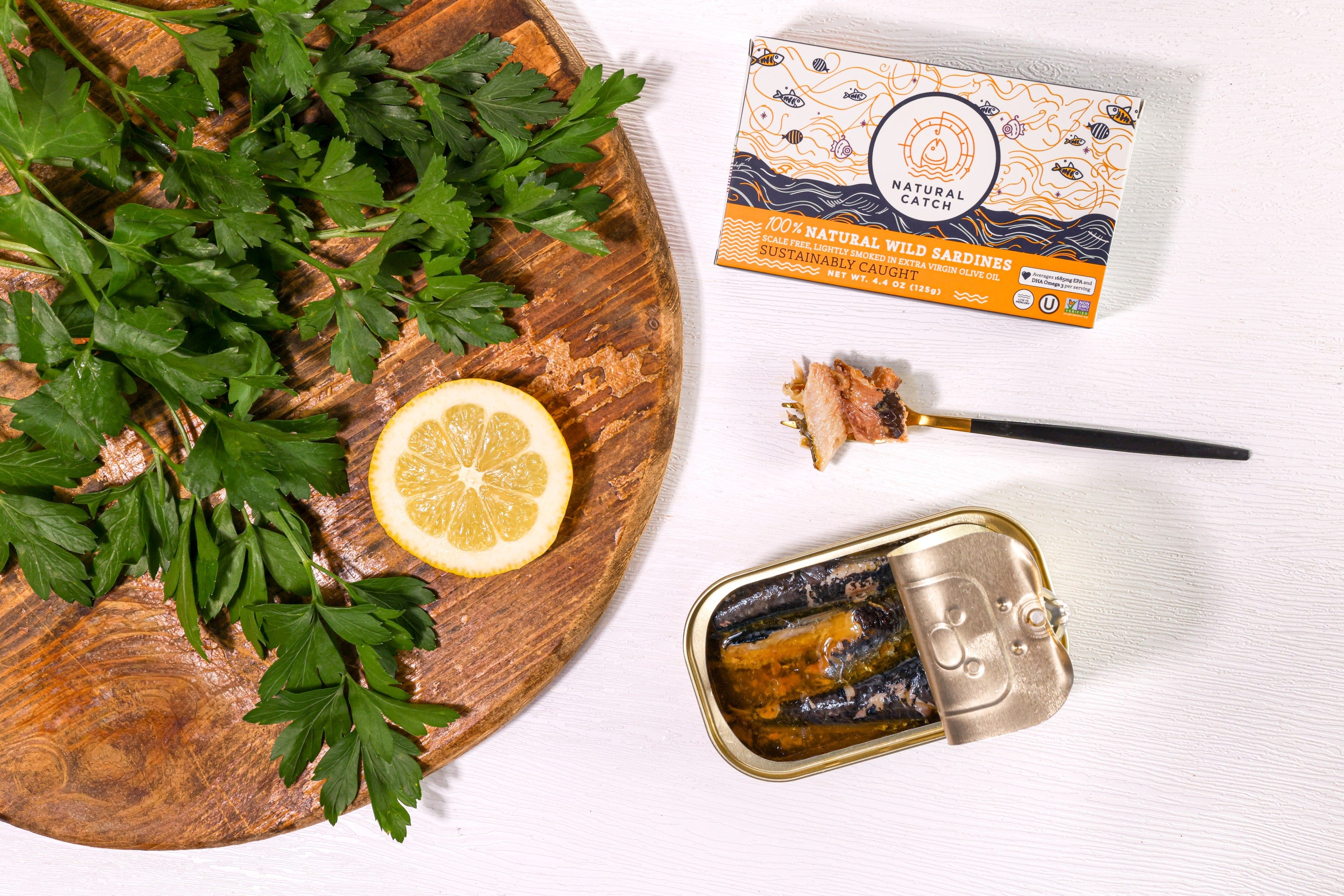 Open can of Natural Catch Sardines with a fork, parsley and lemon on a wood board
